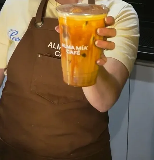 Un Pumpkin Cloud Latte frío en vaso de Alma Mía, frente al mandil café de la casa